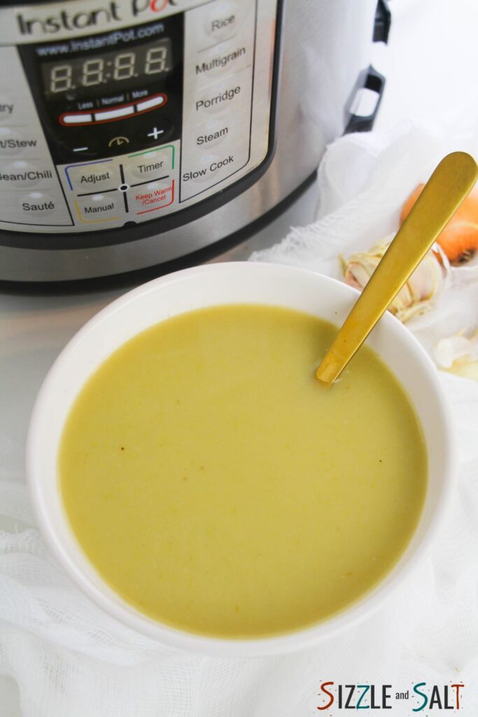 a white bowl filled with silky green asparagus soup with an Instant Pot and aromatics in the background.